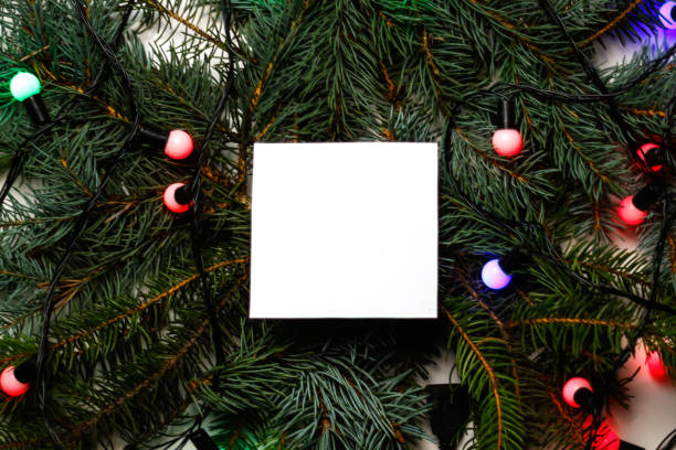 istock Defocus blank white card on natural christmas background with light lamps. Creative layout made of Christmas tree branches with paper card note. Decorative festive frame of branches. Out of focus 1345296694