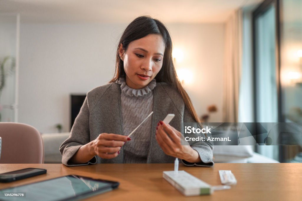 Asian Woman Holding Covid Rapid Test And Waiting For Results Front View Of An Asian Woman Holding Covid Rapid Test And Waiting For Results At Home Coronavirus Stock Photo