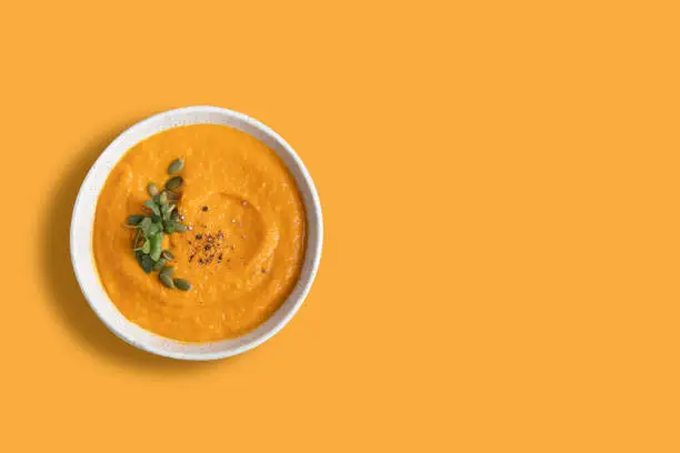 Photo of Pumpkin soup decorated microgreens isolated on orange background.