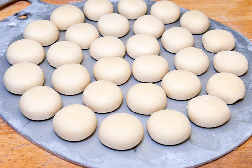 Pre shaped bun dough on a mold tray waiting to get baked. Production line of pre-shaped unbaked rolls on a tray.