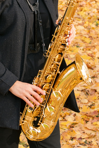 A woman plays a saxophone against a background of yellow leaves in an autumn park. Close-up