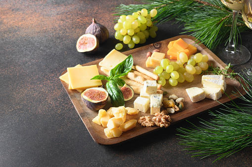 Christmas cheese platter with different cheese and grapes, nuts, olive, figs on a brown background with copy space. Festive holiday appetizer. Close up.