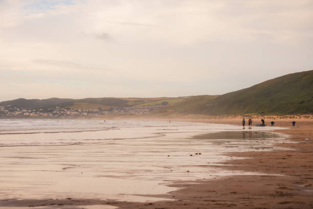 istock Low angle view at the waters edge on a uk beach with people surfing in the background 1345302152