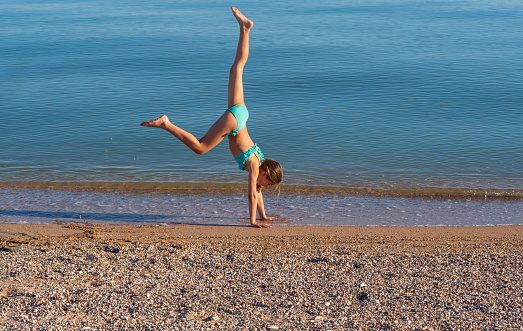 A young woman makes a wheel on the street. acrobatic gymnastics girl in a bikini on the beach. A young woman performing a pose at the water's edge. With space to copy.