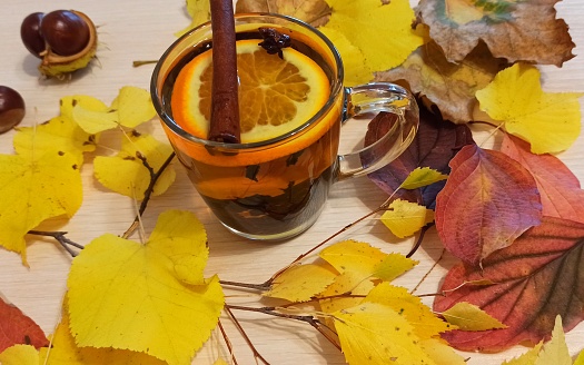 Mug of tea with cinnamon and orange on the table surrounded by yellow leaves, the concept of a cozy tea party in autumn days