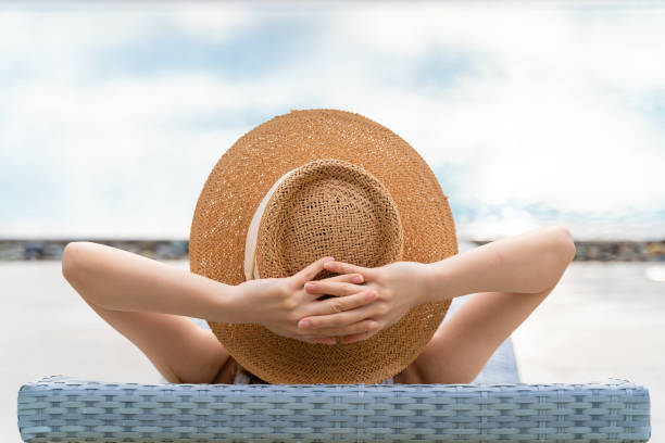 Rearview of a woman in sun hat relaxing at luxury hotel tropical resort swimming pool. Female enjoying summer vacation outdoors. stock photo