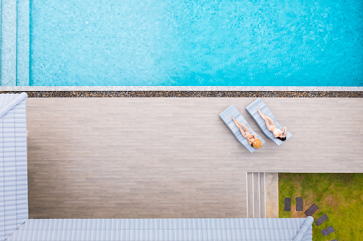 Top view of a slim young woman in hat relaxing in resort swimming pool. Female enjoying sunbathing.
