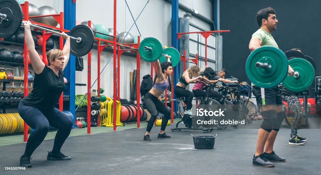 Personas que practican levantamiento de pesas levantando pesas en el gimnasio - Foto de stock de Entrenamiento combinado libre de derechos