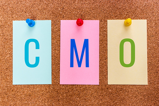 Conceptual 3 letter acronym CMO(chief marketing officer), a corporate executive responsible for marketing activities in an organization, on multicolored stickers attached to a cork board