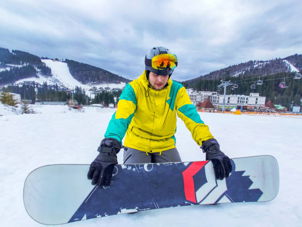 istock man with snowboard sitting at snowed hill 1345310729