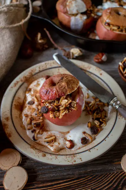 Homemade breakfast for autumn and winter season with a oven baked apple served with fresh granola and yogurt and topped with cinnamon. Served on a rustic plate on wooden table. Closeup from above. Vertical image