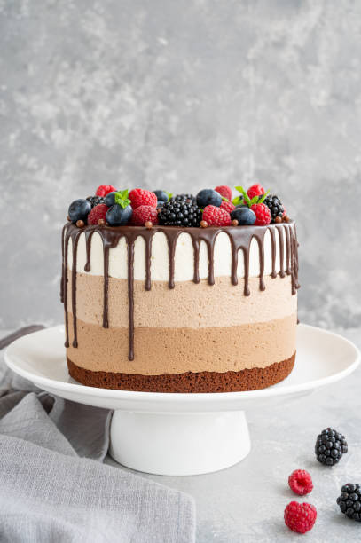 istock Three chocolate mousse cake with chocolate glaze, blueberries, raspberries and blackberries on top on a white plate on a gray concrete background. Cake with three layers of different taste. Copy space. 1345313577