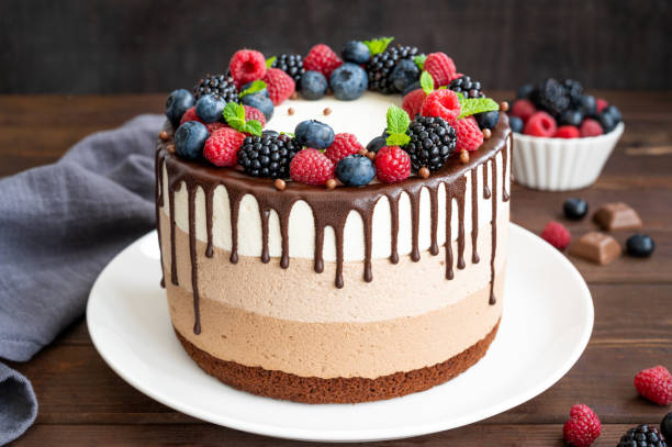istock Three chocolate mousse cake with chocolate glaze, blueberries, raspberries and blackberries on top on a white plate on a dark wooden background. Cake with three layers of different taste. Copy space. 1345313592
