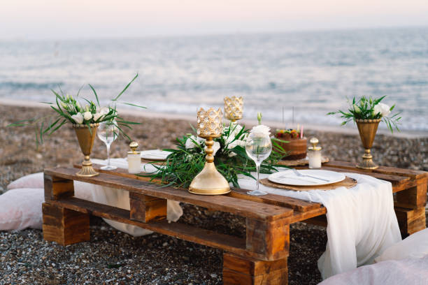 istock Festive table setting. Luxury decorated table for a romantic date. Festive details tablecloth, candles, plates, glasses on beach background. Table decor. Catering  for a romantic date. 1345314572