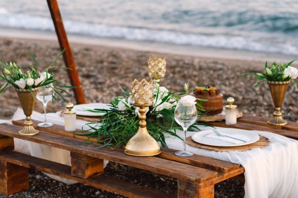 istock Festive table setting. Luxury decorated table for a romantic date. Festive details tablecloth, candles, plates, glasses on beach background. Table decor. Catering  for a romantic date. 1345314665