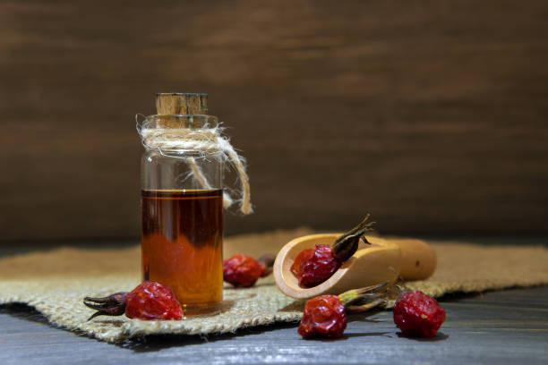 Rosehip oil on wooden background with red fruits The rose hip oil on a wooden boards against a dark background. Bottle tied with a cord with dogrose essential oil. wild rose hip stock pictures, royalty-free photos & images