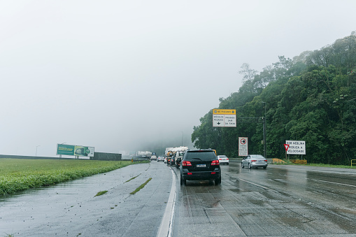 São Paulo, Brazil - September 30, 2021: Under fog, slow down. Imigrantes highway: Intense traffic with rain and fog. A billboard asks you to respect speed limits.