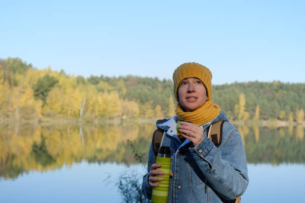 istock Mature woman is resting and drinking tea while walking in autumn nature park 1345323366