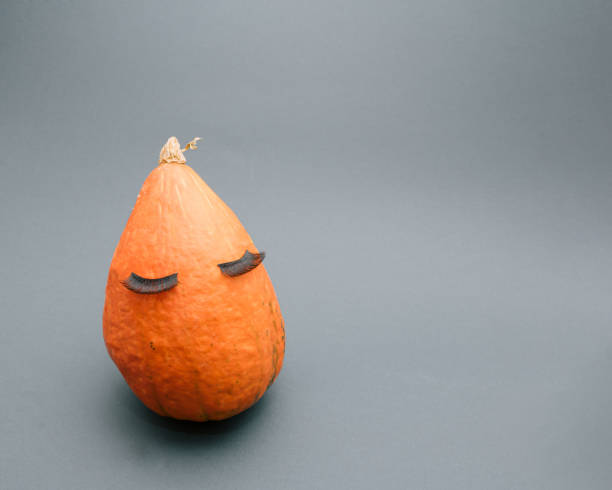 istock Pumpkin with false eyelashes ready for Halloween season. Minimal creative idea for autumn October on gray background. 1345323472
