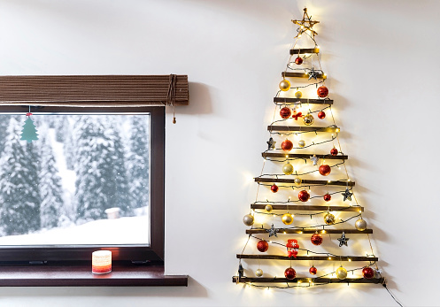 Christmas tree made of wood hanging on the wall, winter snowy landscape outside the window