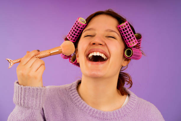 istock Woman with hair curlers while applying makeup with a brush. 1345325136