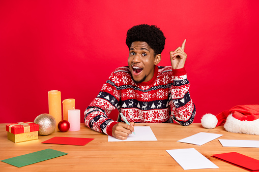 Photo of young impressed brunet guy sit write point up wear holiday sweater isolated on red color background