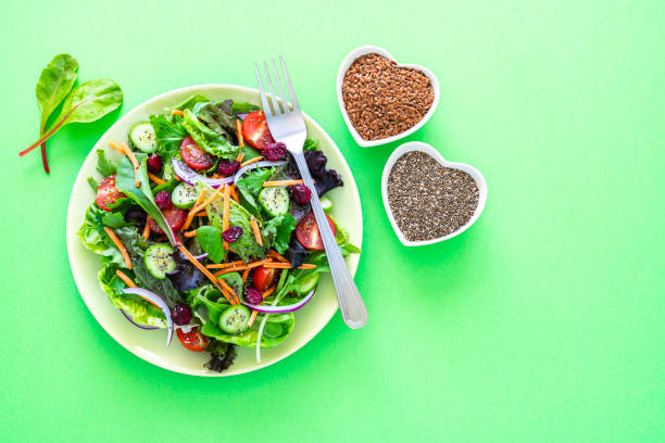 Overhead view of a healthy fresh organic salad plate shot on green background. Two heart shaped bowls with chia seeds and flax seeds are next to the salad plate. The composition is at the left of an horizontal frame leaving useful copy space for text and/or logo at the right.\n High resolution 42Mp studio digital capture taken with SONY A7rII and Zeiss Batis 40mm F2.0 CF lens