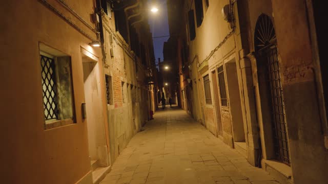 Silhouettes of people walking in narrow Venetian street