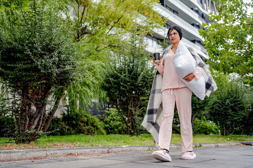 Mujer de negocios sosteniendo almohada y caminando en pijama y zapatillas photo