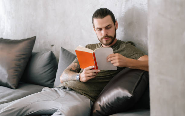 istock Millennial handsome bearded hipster holding and reading book while sitting sofa in cafe relax time on holiday. Holiday activity and lifestyle concept. 1345334902
