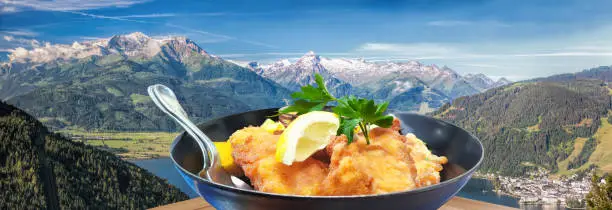 Traditional austrian food (Wiener schnitzel) over Zell am see village with Kitzsteinhorn peak ( Tauern Alps) in Austria