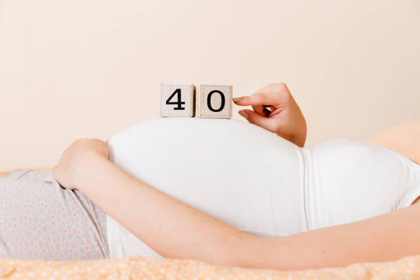 pregnant woman in white underwear on bed in home holding calendar with weeks 40 of pregnant. maternity concept. expecting an upcoming baby - pregnant count stockfoto's en -beelden