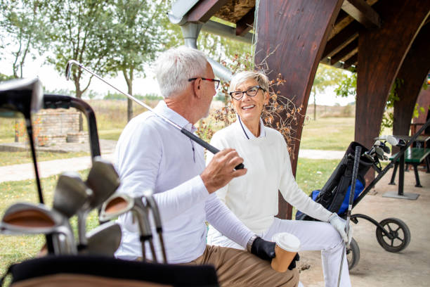 starsi ludzie na emeryturze rozmawiają i śmieją się przed treningiem golfowym. - golf green practicing sports training zdjęcia i obrazy z banku zdjęć