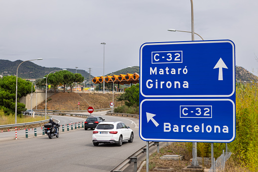 Maresme, Catalonia, Spain - September 27th, 2021: Direction blue highway sign to Barcelona, Girona and Mataró, cars and motorcycle driving towards a toll booth highway, on September 27th, 2021.