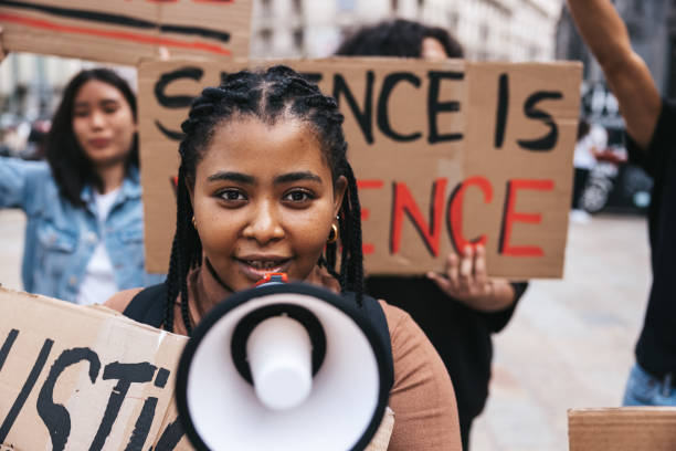 Young woman shouting on megaphone during a protest People united against racism. Anti-Racism protest. Protestors holding hand-made signs on cardboards and marching together in the city streets in downtown. police brutality photos stock pictures, royalty-free photos & images