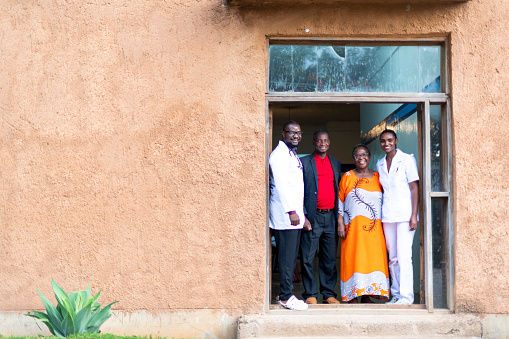 Happy African doctor and nurse standing with senior couple in hospital doorway