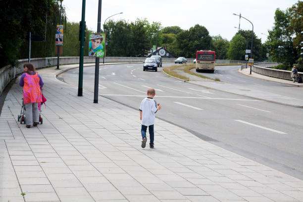Street Ruhrtalstrasse in Essen Werden. On street is a few traffic and a bus is leaving into back. A woman with baby carriage is walking at left side. A boy in german football trikot is following slowly.