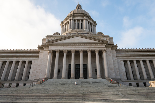 Olympia, USA – Sep 19, 2021: The Washington state Capitol house in Olympia early in the morning as a woman kneels and prays on steps.