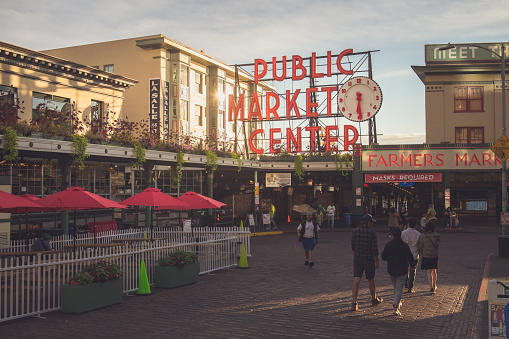 Seattle, USA - Sep 13, 2021: Late in the day the sun reflecting at the iconic public market sign at Pike Place Market. as people pass by.