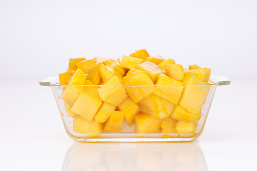 Ripe Mango cubes or cut piece arranged in a glass square container with white color background.