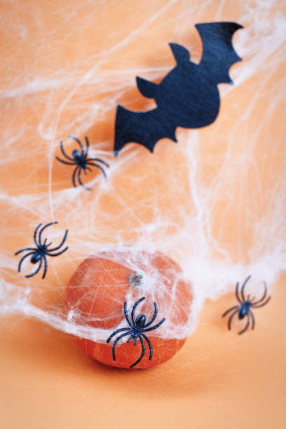 istock Halloween pumpkin with spider web, bat and black spiders on orange background. 1345360327