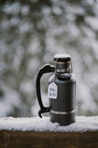 un growler pieno di birra fredda siede sulla ringhiera di legno innevata all'esterno - bitter beer bottle alcohol beer foto e immagini stock