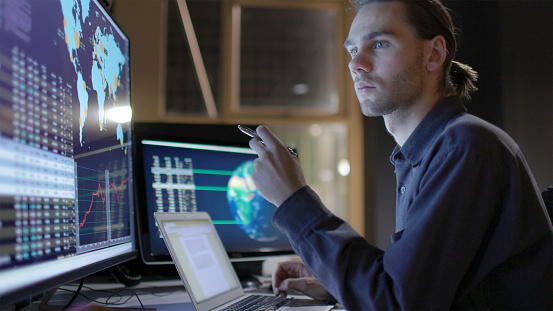 Stock photograph of a young man working with a large computer monitor, He’s studying global data with maps of the Earth.