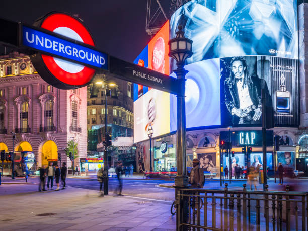 Underground sign illuminated by the neon billboards of Piccadilly Circus and Regent Street in the busy heart of London, UK.