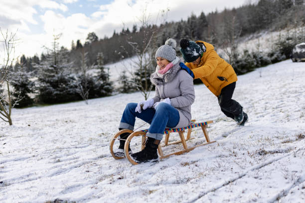 kleiner junge schiebt seine mutter an einem wintertag auf einen schlitten - little boys sled clothing slide stock-fotos und bilder