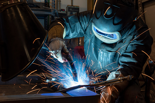welder with protective mask welding metal and sparks. Industrial steel welder in factory.