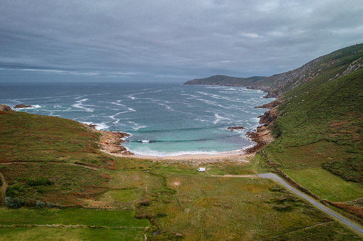 Drone aerial view of a camper van on a wild beach with green landscape in Galicia, Spain