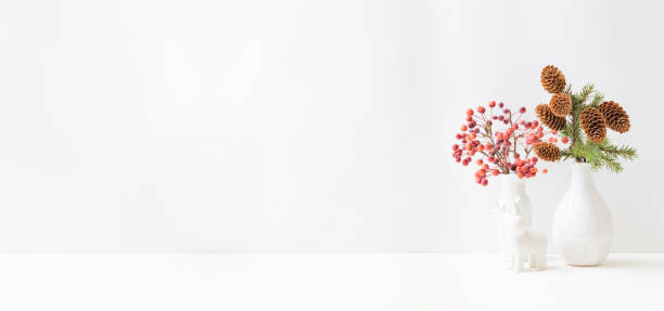 istock Home interior with decor elements. Small red apples in a vase and branches of spruce with cones on a light background 1345371736