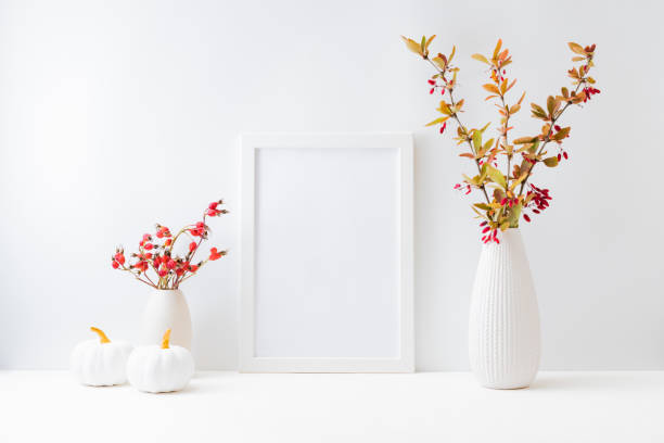 istock Home interior with decor elements. Mockup with a white frame, colorful autumn leaves and red berries in a vase on a light background 1345371769