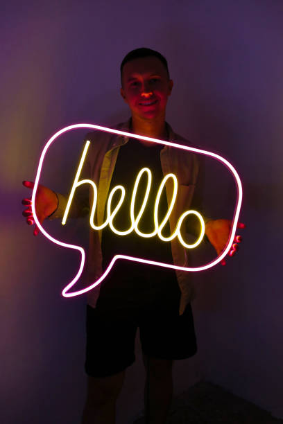 Handsome young man holding pink and yellow neon sign hello.